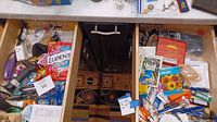 Photo shows two open drawers with assorted kitchen, household and miscellaneous items including medicine packets, keys, lighters, kitchen utensils, and other small objects.