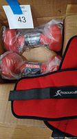 Box containing two new 6lb red vinyl dumbbells and one Prosource red ankle weight with black strap.