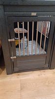 Front view of the EcoFlex dog crate showing metal bars on door and interior pad with dog product bottles inside.
