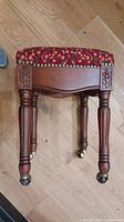 Top view of the embroidered padded seat and carved wooden legs of the stool.