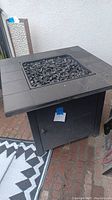 Photo showing the square table height fire pit with black fire rocks recessed in the top surface, with tiled edge and black base.