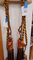 Photo of two giraffe head drapery tiebacks with long fringe hanging by yellow and black twisted cords.