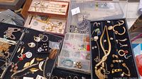 Plastic sorting case open showing multiple compartments filled with gold-tone rings, earrings and small jewelry pieces