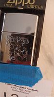 Close-up of the Marlboro Zippo lighter logo etched on a polished silver surface, showing the cowboy design.