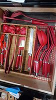 Photo showing drawer with red kitchen utensils organized in baskets, including spoons, knives, brushes, and spatulas.