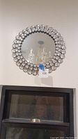 Full front view of the round mirror hanging on a wall, showcasing the clear reflective surface and rhinestone frame with graduated sizes.
