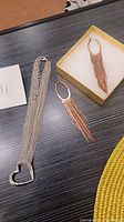 Full view of the necklace laid flat next to the pair of brass fringe earrings in a box.