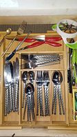 Top drawer showing Korean silverware with textured handles organized in a wooden drawer organizer alongside metal tongs and other utensils.