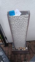 Front view of the tall rectangular fountain with faux pebble surface and real stones at the base.