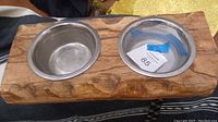 Front view of wood log pet bowl holder with two metal bowls inserted, showing smooth wood grain and metal bowl interiors with slight wear