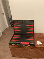 Photo of opened black folding backgammon board case showing red and green triangles and stacked playing pieces on either side.
