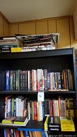 Black bookshelf with books on two shelves and books stacked on top including economic and football titles