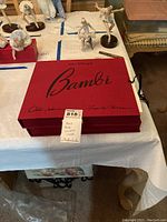 Two red cloth-bound Bambi folio cases stacked on table with other collectibles visible