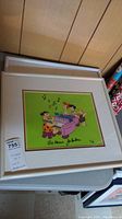 Framed Flintstones print front view with green background, pink piano, stone-age characters and Hanna-Barbera signatures visible