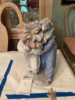 Front view of the Lladro porcelain figurine showing the couple embracing, with a white and pink ruffled collar on the female and blue costume on the male.