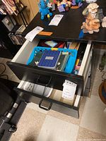 Photo showing two opened drawers containing various office supplies, papers, and a blue Fossil tin.