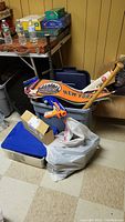 Photo of sports pennants, Nerf gun, baseball bats, and assorted objects in plastic bins and bags in basement