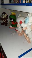 Four Looney Tunes character figures (Taz, Marvin the Martian, The Brain, Pinky) on shelf