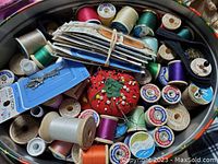 Thread spools, pin cushion with pins, and packaged notions in a bin
