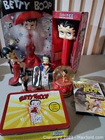 Photo of Betty Boop collectibles including large boxed figurine, giant Pez dispenser, snow globe, tin lunch box, and several smaller figurines and accessories.