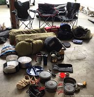 View of camping chairs, sleeping bags, tent, cookware, and assorted gear arranged on concrete