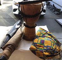 Photo showing the carved wooden djembe drum, the leather pieces rolled, and the vibrant patterned carrying bag.