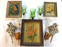 Top-down view of all lot items including two ornate metal wall sconces with interchangeable green, amber, and clear glass shades, and three framed floral paintings signed Malisa.