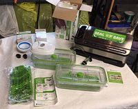 FoodSaver vacuum sealer and accessories laid out on a table, including storage containers, vacuum hose, sealing glove, and user manual.