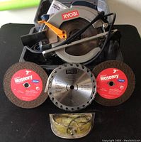 Top-down view of Ryobi circular saw, two Norton FastCut masonry blades, one Ryobi circular saw blade, and safety glasses.