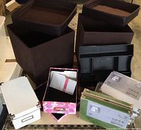 Photo of 3 brown foldable storage cubes with faux leather tops, 3 boxed IKEA KASSETT metal storage boxes in green packaging, 2 assembled IKEA KASSETT boxes, and black compartmentalized storage tray.