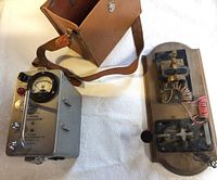 General view of scintillator device with analog meter, control knobs, handle, leather carrying case, and separate mounted electrical apparatus.