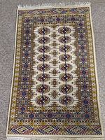 Full view of beige area rug with geometric medallion and multi-colored borders.