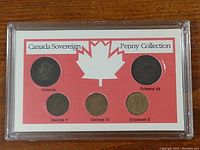 Full view of Canadian Sovereign Penny Collection display case with five pennies mounted and labeled under each monarch name with a maple leaf graphic on red and white background.