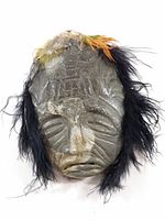 Front view of carved stone face with feather adornments