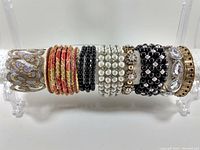 Front view of all thirteen bracelets displayed on a clear stand showing different styles and colors