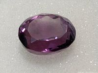Close-up of a dark purple oval cut amethyst gemstone, showing the cut and clarity.