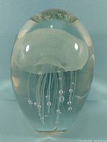 Close-up image of a clear glass paperweight containing a white jellyfish figure with tentacles and air bubble accents inside.