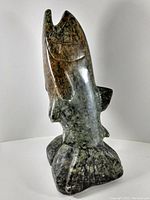 Side view of greenish-gray stone salmon sculpture on carved base