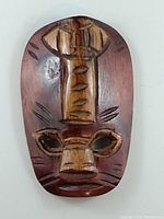Front view of a hand carved wooden mask with lacquer finish showing carved facial features and dark wood tone.