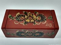 Top view of hand painted wooden box featuring traditional floral folk art motifs, signature 'HB' visible on the side.