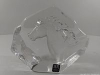Clear lead crystal horse sculpture with horse head carved in relief and labeled with Mats Jonasson sticker on the front base.