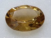 Close-up photo of the oval cut natural citrine with faceted surface on white foam.