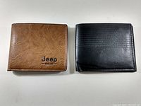 Top view of two closed leather wallets, brown Jeep branded and black wallet side by side