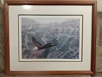 Full view of framed print showing bald eagle in flight over forest and mountains.