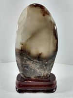 Photo of polished standing stone with color variations and mounted on a reddish wooden base.