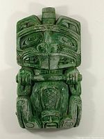 Front view of green stone carving figurine showing wear on green coating and detailed facial/body engravings
