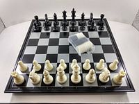 Top-down view of the magnetic chess board with white and black pieces set up and a small cloth pouch containing two rolled items on the board.