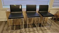 Three black faux leather barstools lined up side by side facing camera