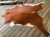 Full view of brown and white cowhide rug laid flat on wood floor
