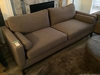 Front angle of the grey sofa against a fireplace, showing full frame, cushions, and legs